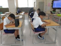 「時間を意識しよう」の活動で、用紙のマス目を色鉛筆で塗りながら、3分の長さを体感する生徒たち。前方の画面には活動の説明が映っている。