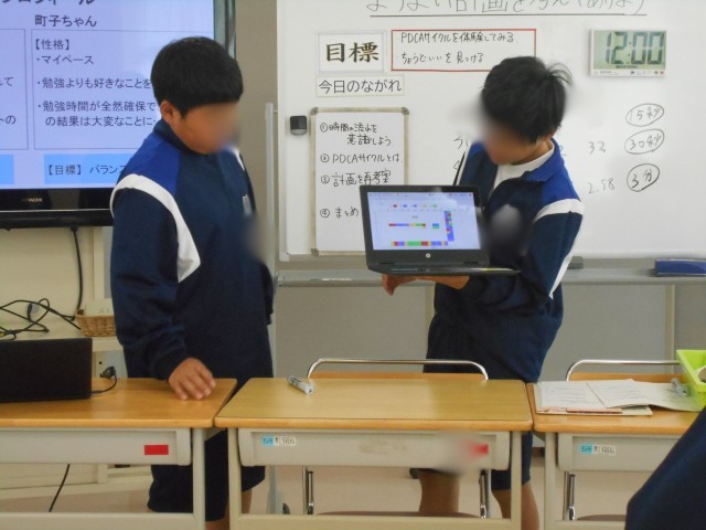 グループで考えた学習計画を、ノートパソコンの画面を見せながら発表する生徒たち。黒板には本時の目標「PDCAサイクルを体験してみる／ちょうどいいを見つける」と授業の流れ、時間の計測結果が記されている。